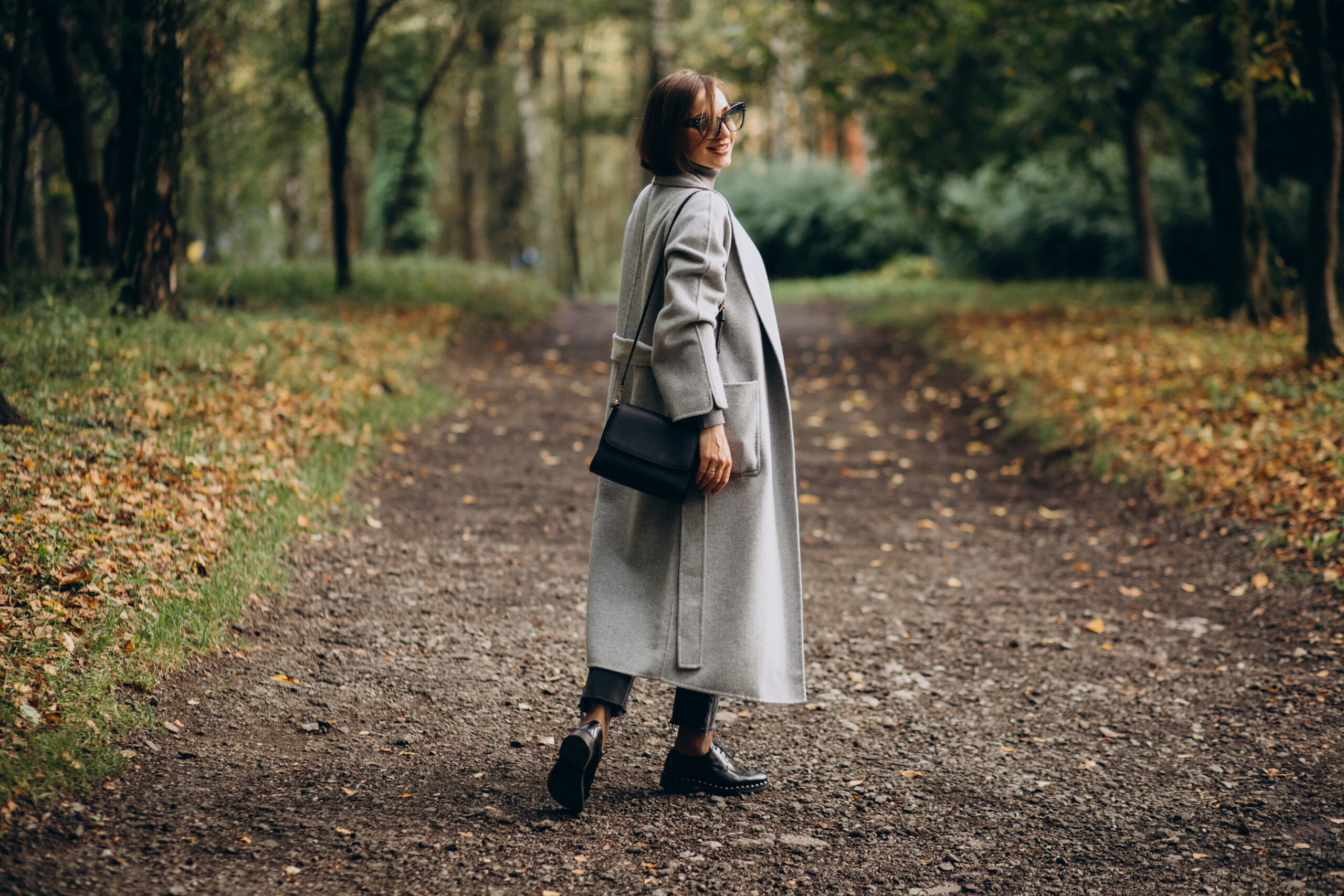 Woman standing alone on a wooded path, dressed for work, pausing in nature to reflect, symbolizing ADHD burnout recovery