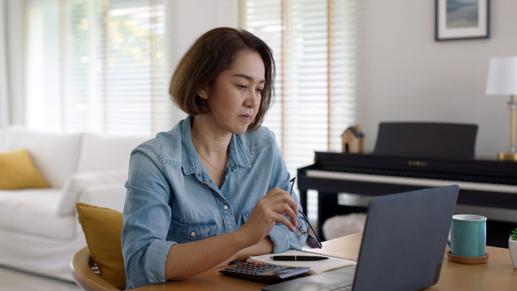 Woman with ADHD looking at laptop, holding glasses, representing the mental effort of deciding what to do with each email