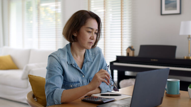 Woman with ADHD looking at laptop, holding glasses, representing the mental effort of deciding what to do with each email