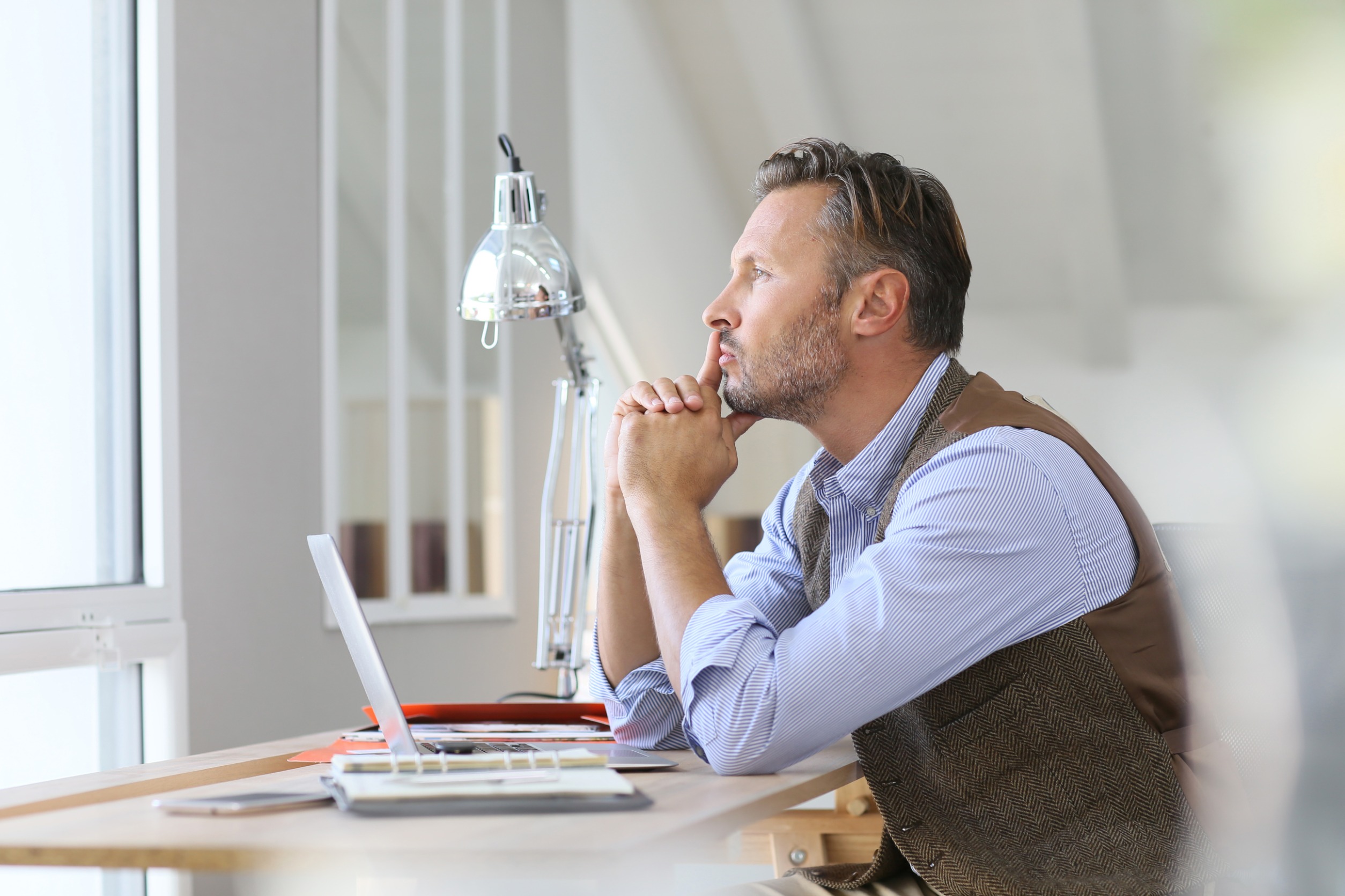A middle-aged man with ADHD looks thoughtfully out a window, reflecting on how to become a more effective manager and leader.
