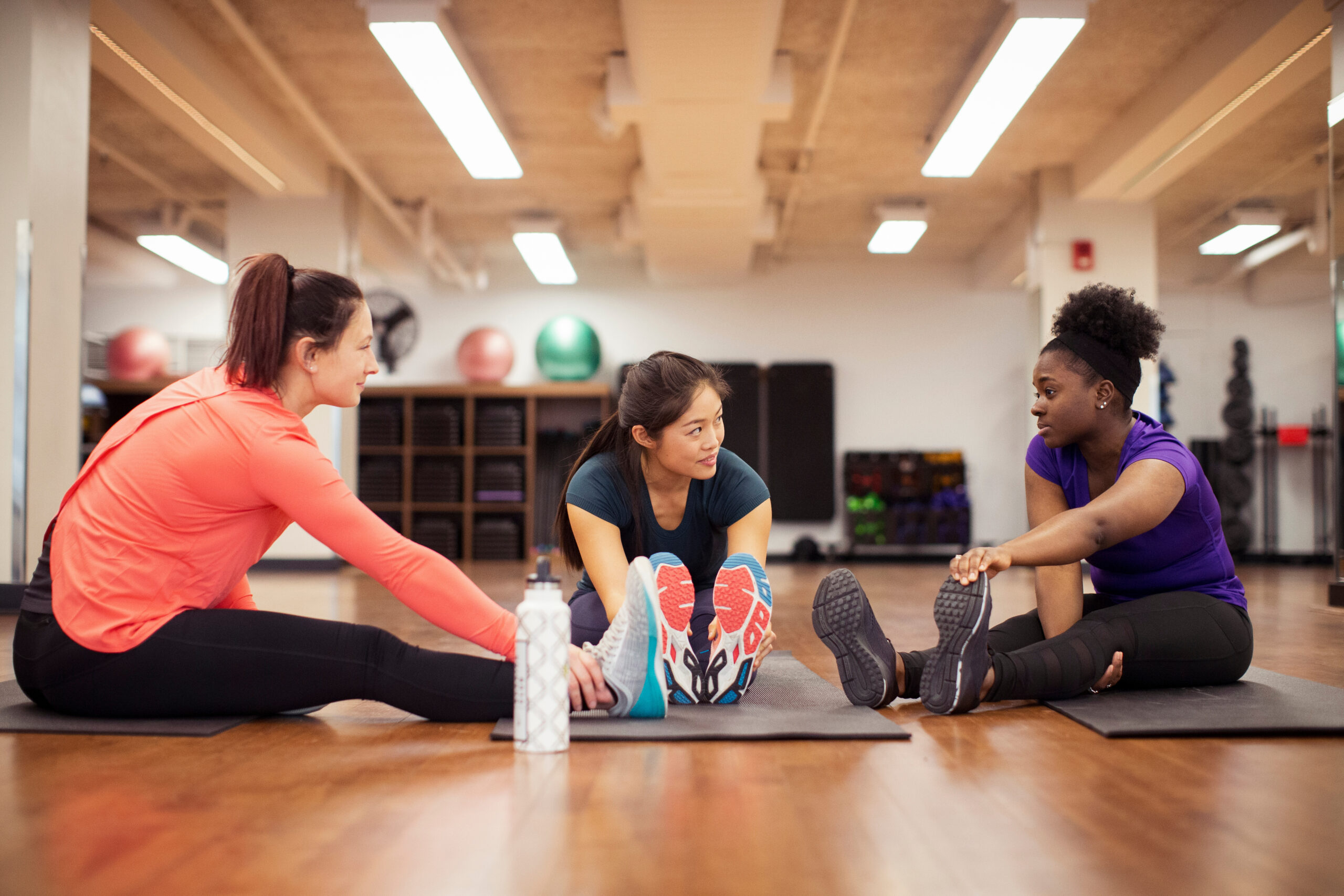 Three women stretching on gym mats demonstrate ADHD and willpower strategies like accountability, body doubling, and fixed time.
