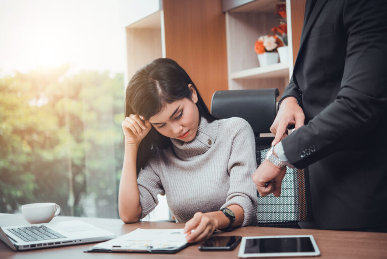 High-functioning adult with ADHD shown as a professional woman at her desk taking notes while her boss points to his wristwatch, symbolizing time pressure, decision fatigue, and hidden challenges.