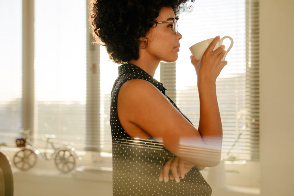 ADHD adult pausing to reflect on whether to follow through on a task, holding a cup of coffee by a window