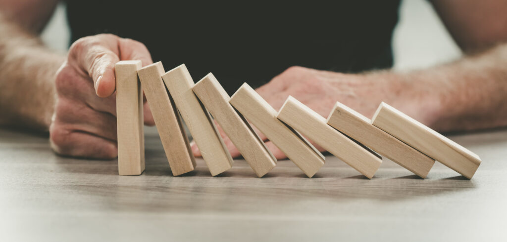 Person stopping falling dominoes with their hand, representing proactive planning and intentional decision-making with ADHD