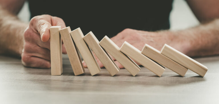 Person stopping falling dominoes with their hand, representing proactive planning and intentional decision-making with ADHD