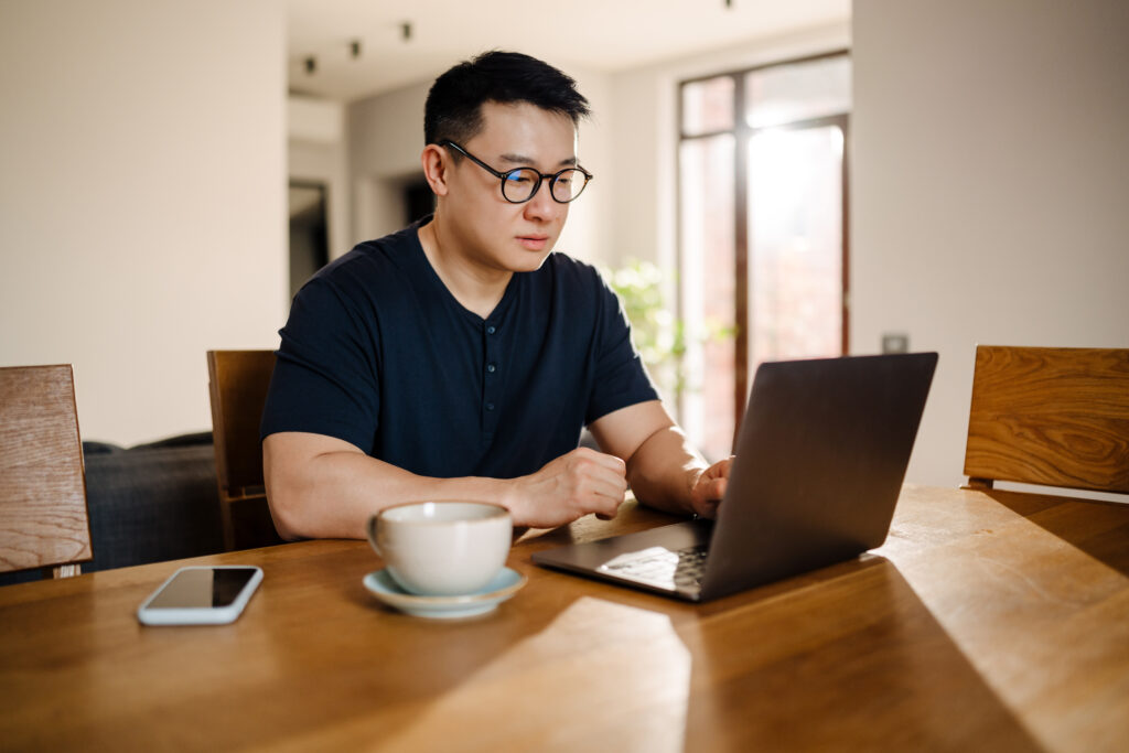 Man working on a laptop at a wooden table, focused on work, representing ADHD adults navigating job performance and workplace demands.
